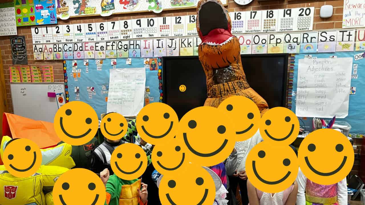 Ms Davis as a T-Rex Dinosaur with her students, their faces hidden behind smiling emojis.