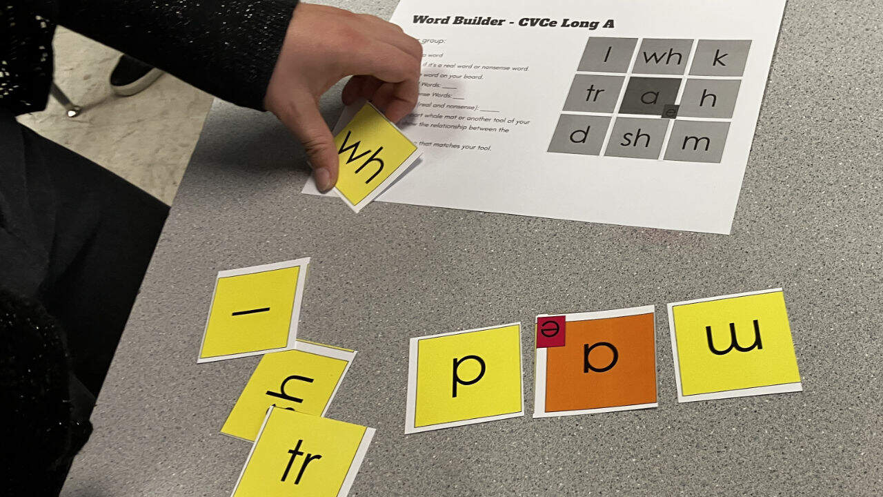 Hands-on phonics activity using letter cards to build words during a math and literacy workshop.